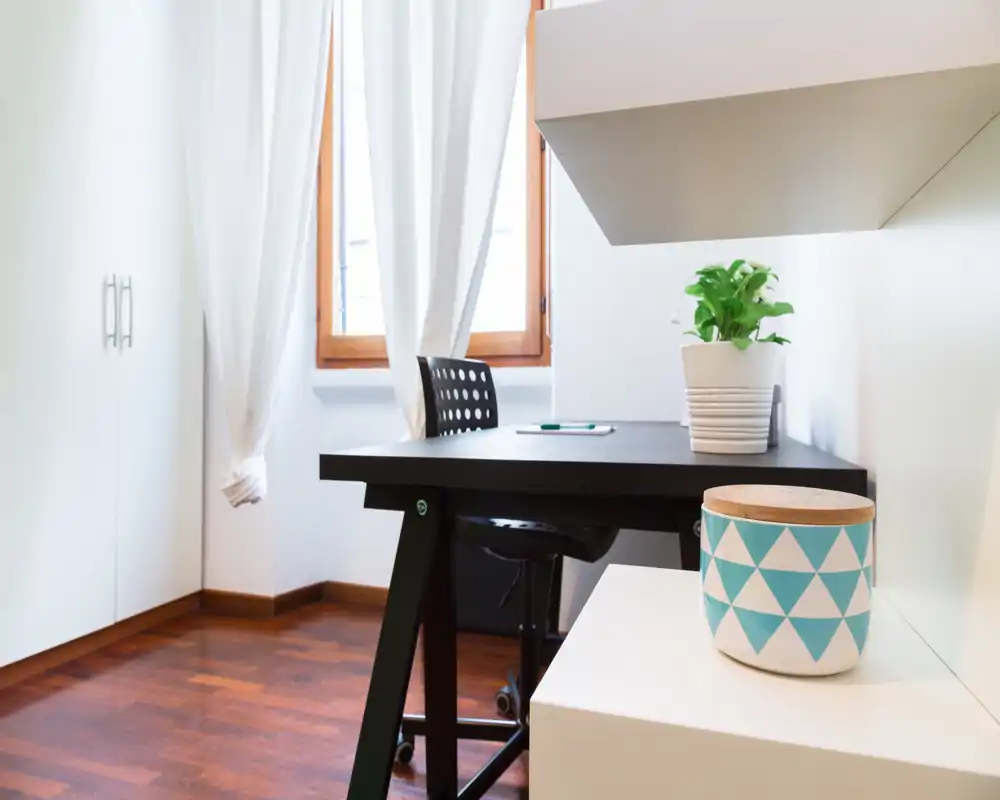 Angolo luminoso moderno per lavoro/soggiorno con scrivania nera, sedia e dettagli decorativi semplici che creano un ambiente curato e funzionale.