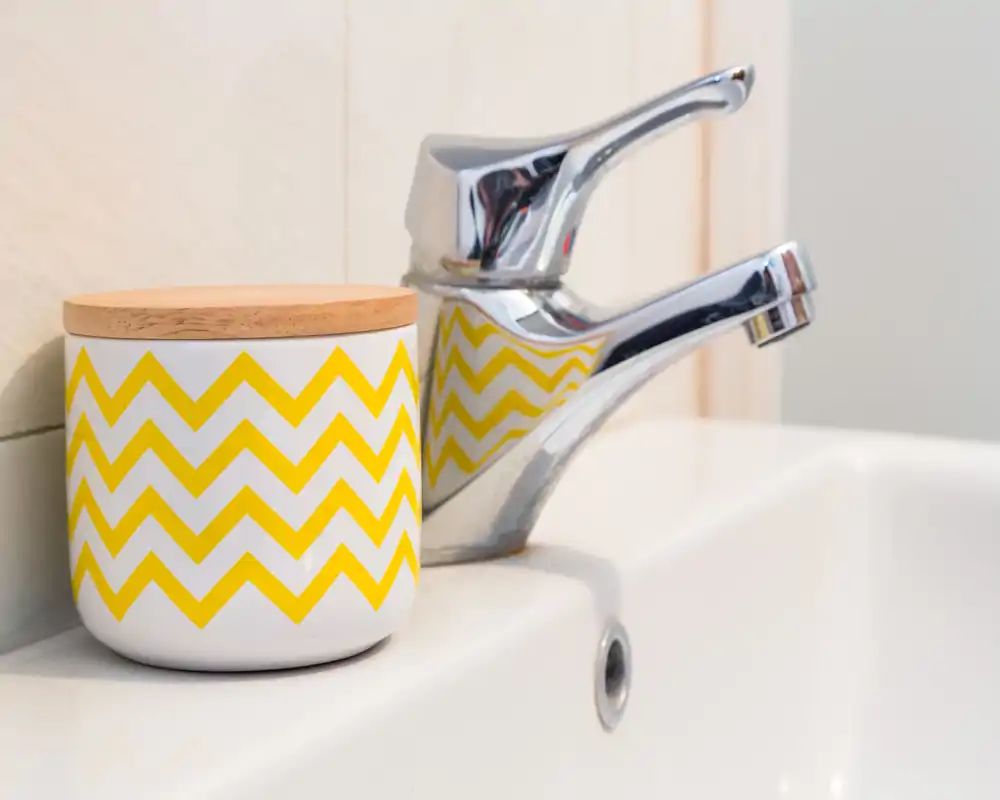 Primo piano del rubinetto del lavabo e di un contenitore decorativo con motivo a zigzag giallo, con superfici in ceramica pulite e finiture cromate.