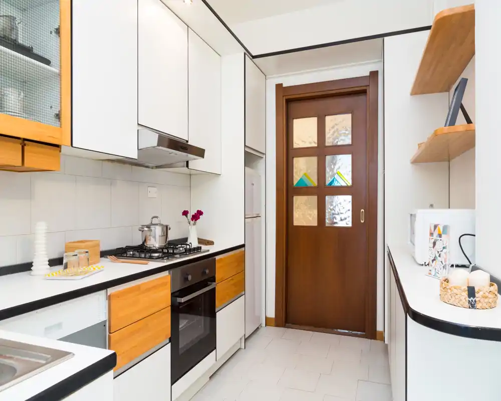 Cucina moderna e luminosa a corridoio con mobili bianchi, frontali dei cassetti in legno caldo, forno integrato e piano cottura a gas — ordinata, ben illuminata e curata per annunci.