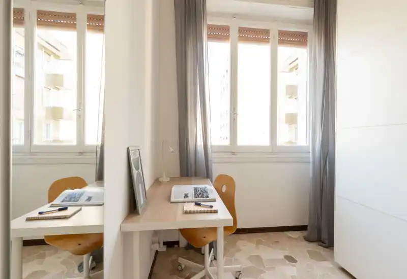 Small, bright bedroom corner set up as a workspace with a desk, chair and large windows letting in natural light.