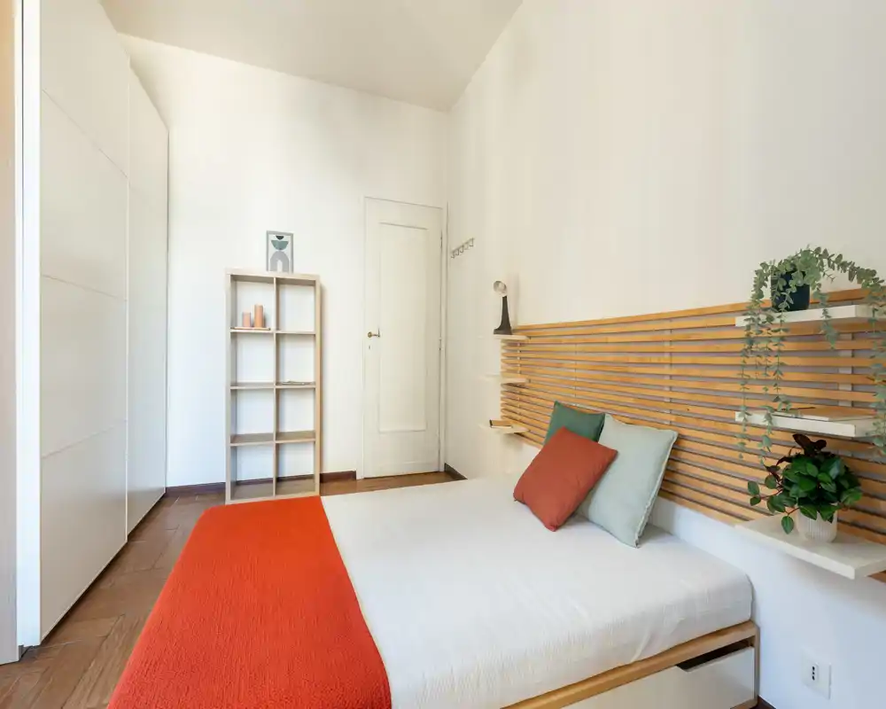 Camera da letto luminosa e moderna con testiera a listelli in legno, biancheria bianca e cuscini colorati — perfetta per annunci che valorizzano stile e comfort.