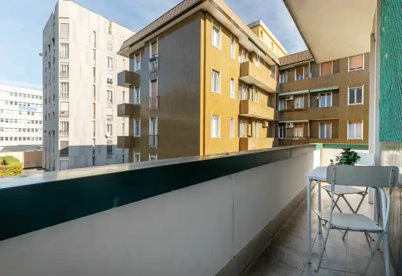 Sunny narrow balcony with a small bistro table and chairs, tiled floor and views over neighboring apartment buildings — ideal for morning coffee.