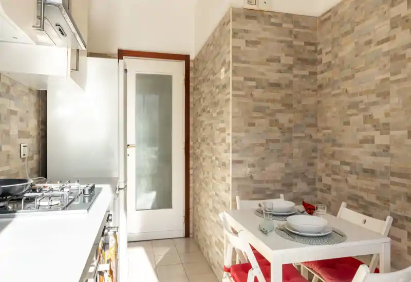 Bright, modern kitchenette with a gas stove, compact dining table and textured stone-look wall tiles — ideal for a cozy urban apartment.