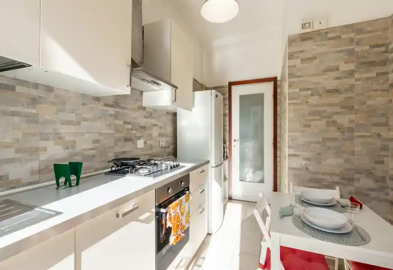 Bright modern kitchen with a gas hob, built-in oven and a small dining nook. Neutral tile backsplash and white cabinetry create a fresh, airy atmosphere ideal for rental listings.