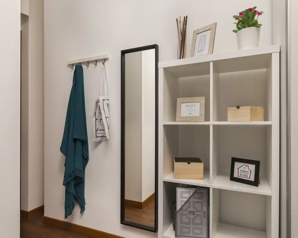 Entrada luminosa y ordenada con percheros, espejo de cuerpo entero y estantería modular: un recibidor práctico y acogedor para abrigos y pequeños objetos.