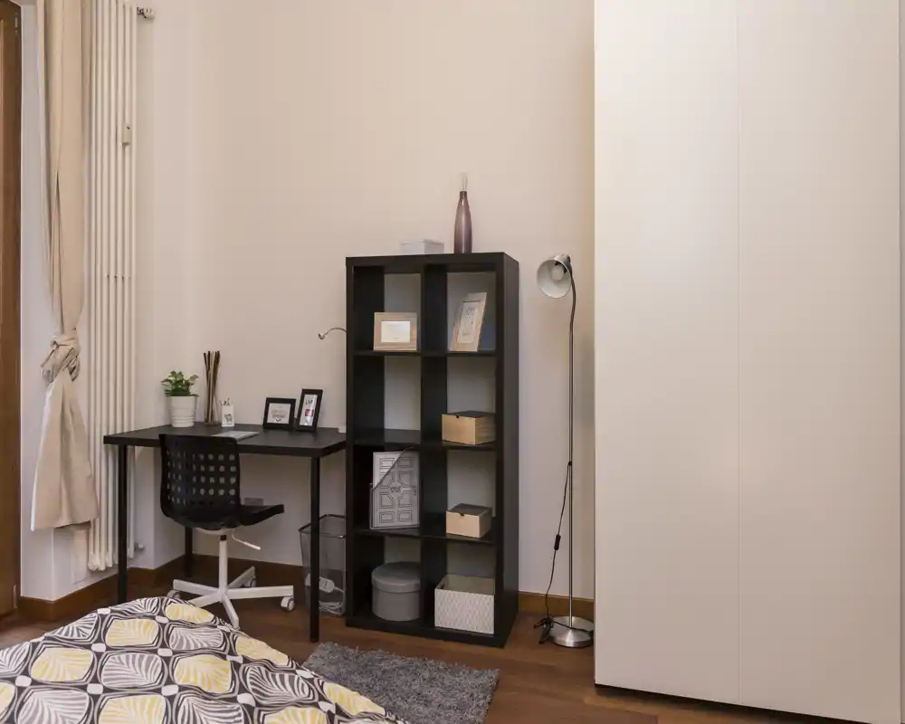 Angolo camera luminoso e accogliente con copriletto a motivi, scrivania compatta e libreria: perfetto per una persona o uno studente.