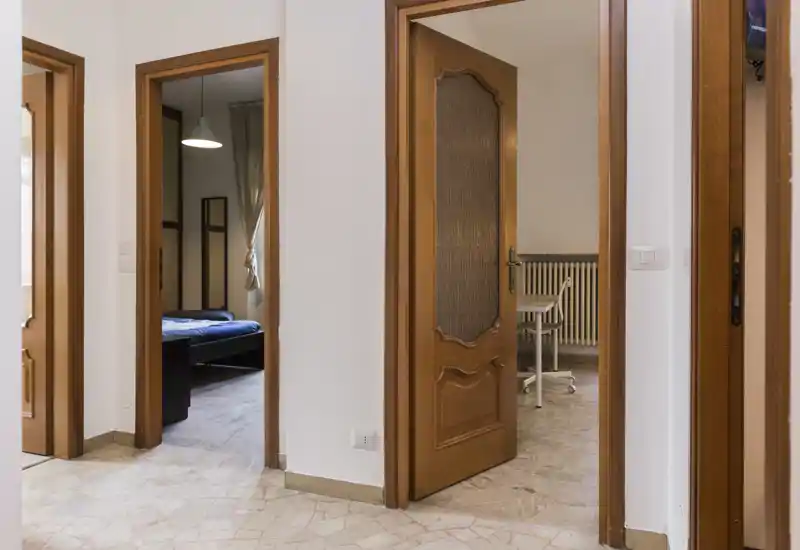 Ingresso/corridoio luminoso con diverse porte in legno aperte verso le stanze adiacenti; pavimento effetto marmo e pareti neutre creano un passaggio pulito e accogliente.