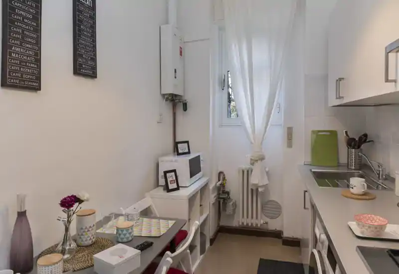 Angolo cottura compatto arredato con lavello singolo, piano di lavoro, microonde e un piccolo tavolo apparecchiato per due — luminoso, ordinato e ben decorato.