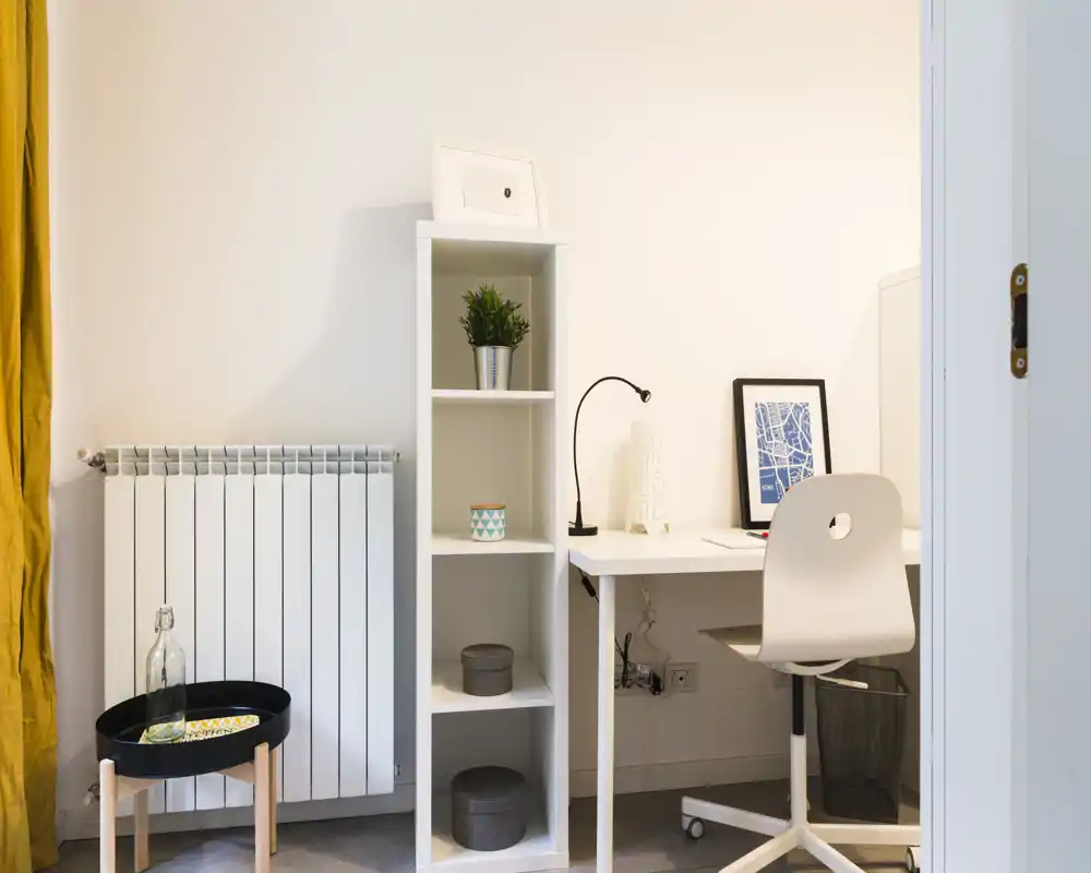 Angolo luminoso e minimale con scrivania bianca, scaffale e sedia confortevole — ideale come piccolo spazio studio all'interno del soggiorno.