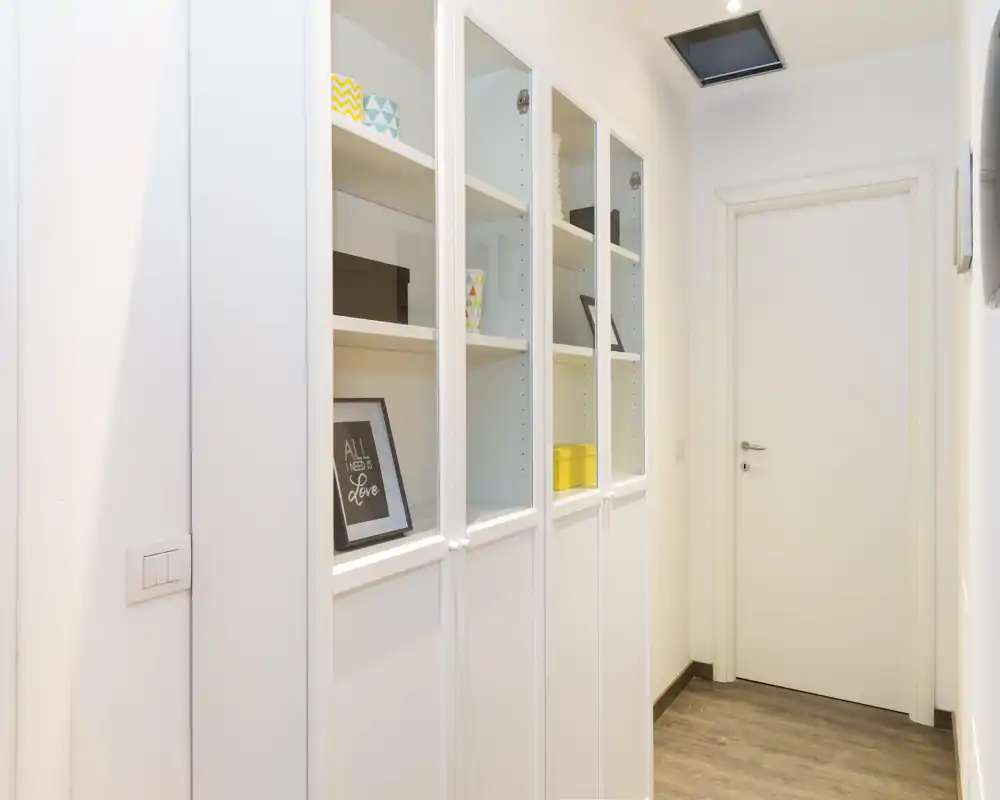Ingresso luminoso e ordinato con armadi a muro bianchi e porta chiusa in fondo; pavimento in legno e finiture moderne che offrono una prima impressione accogliente.