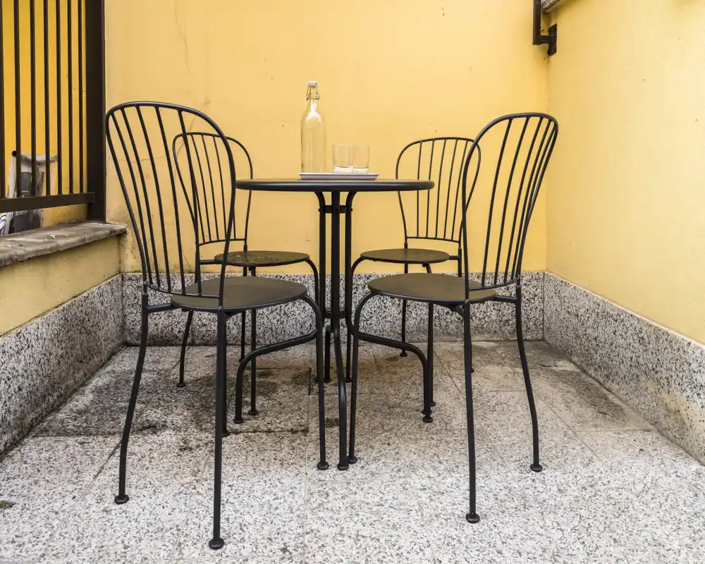 Piccola terrazza privata con tavolino rotondo in metallo e quattro sedie abbinate contro pareti gialle calde; ideale per un caffè mattutino o un aperitivo serale.