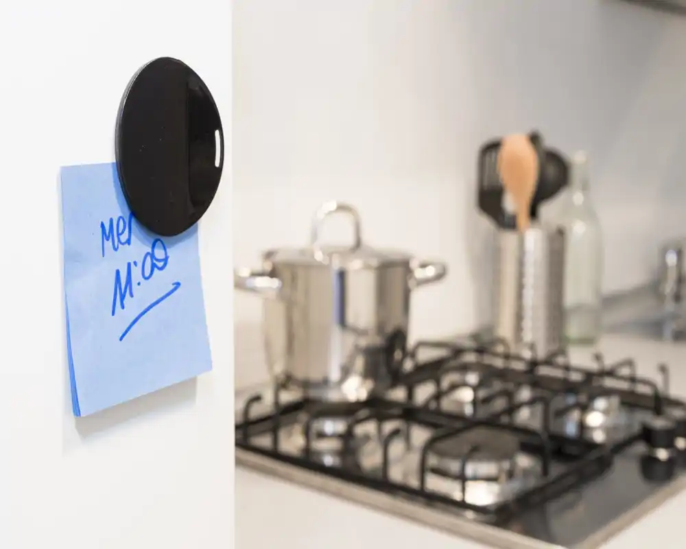 Primo piano di una cucina moderna con pentola in acciaio sul fornello, portautensili e un memo magnetico sul frigorifero; ambiente pulito e luminoso.