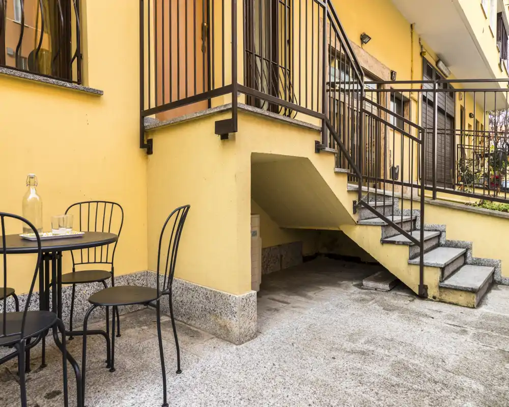 Terrazza privata soleggiata con tavolino e sedie in metallo, pavimento in pietra e scala esterna — ideale per colazione all'aperto o piccoli incontri.