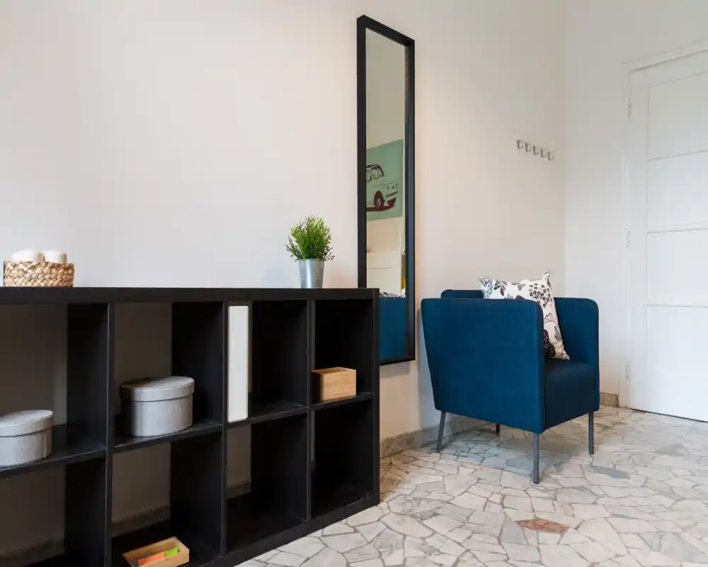 Bright, tidy entrance with a modern blue armchair, wall mirror and black cubby shelving — a welcoming foyer corner.