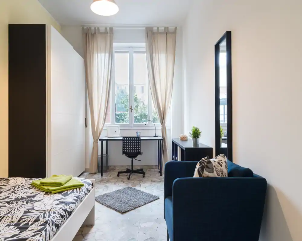 Bright, well-styled bedroom with a single bed, desk by the window and a comfortable armchair — ideal for study and relaxation.