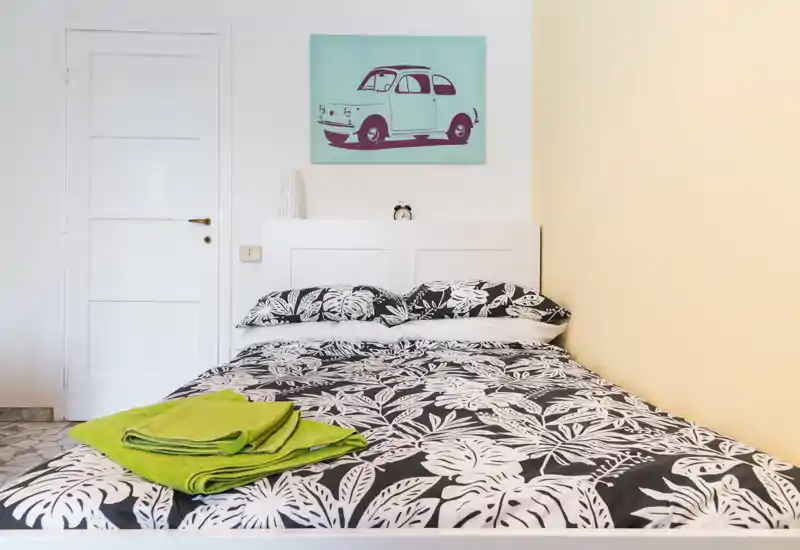 Bright, neatly styled bedroom with a patterned double bed, headboard, and simple wall art. Fresh towels are placed on the bed, creating a tidy and welcoming feel for guests.