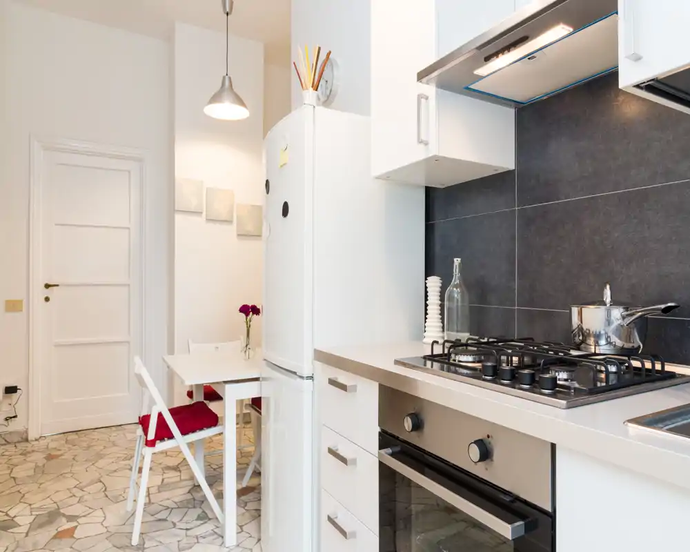 Bright modern kitchen with a gas hob, built-in oven and a small dining nook. Clean white cabinets and dark backsplash create a contemporary contrast.
