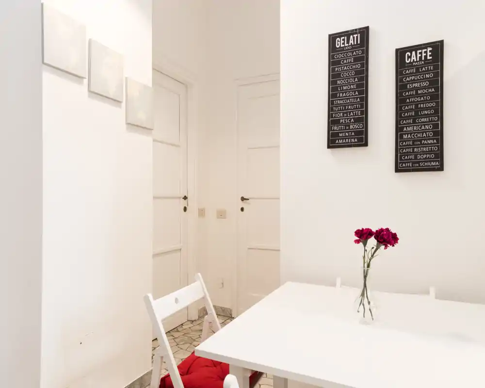 Bright, minimalist dining corner with a white table, folding chairs and a simple vase of flowers—ideal for compact city apartments.