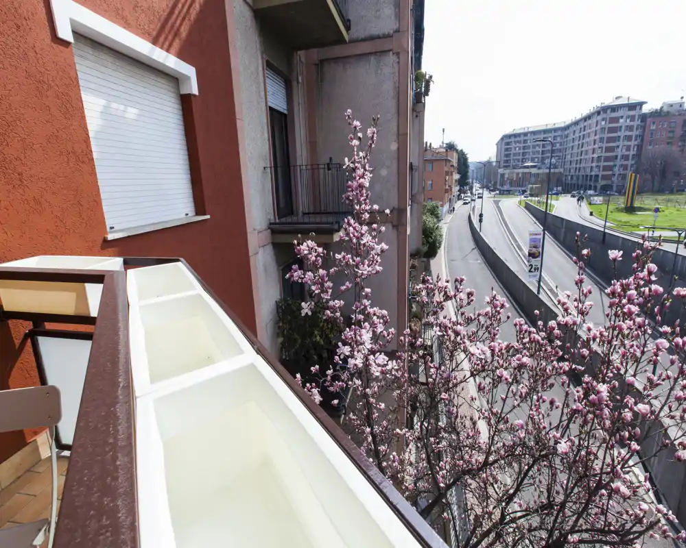 Sunny balcony view with flowering tree and city street beyond; a small outdoor space suitable for morning coffee and city watching.