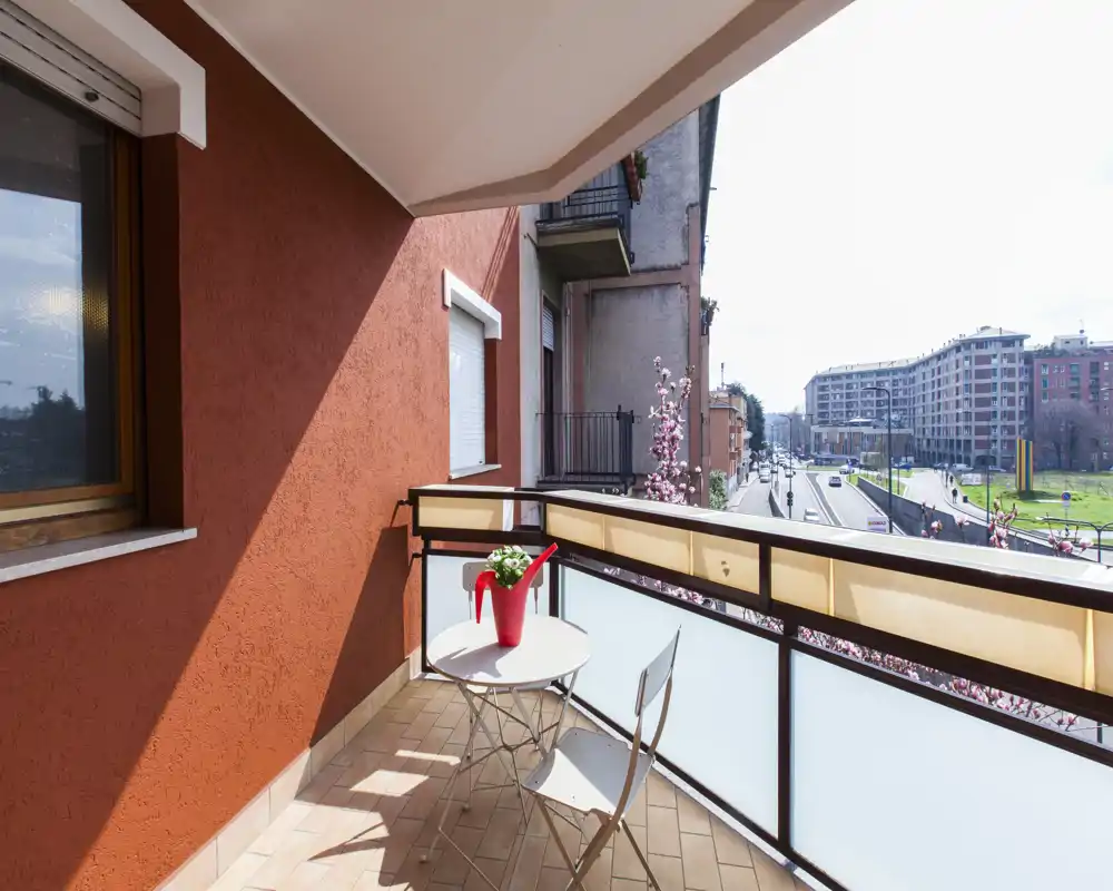 Sunny private balcony with a small table and two chairs overlooking a city street and green area — ideal for morning coffee.