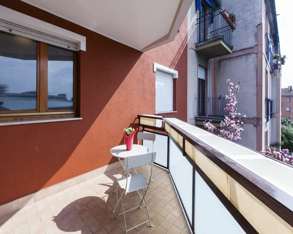 Sunny balcony with a small table and two chairs, ideal for morning coffee. Frosted glass railing and potted flowers create a pleasant, private outdoor corner.