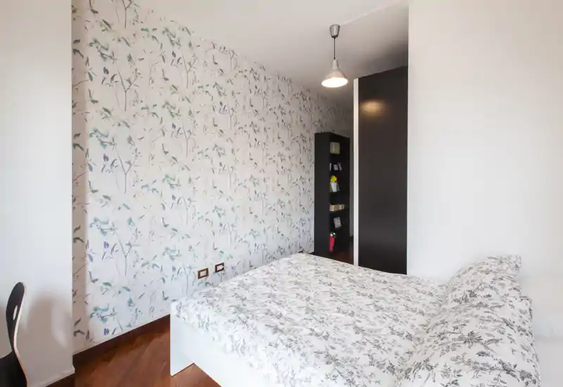 Dormitorio luminoso y bien decorado con papel pintado estampado y una cama doble con ropa de cama floral coordinada. Suelo de madera cálida y luz moderna que crean un ambiente acogedor y elegante.