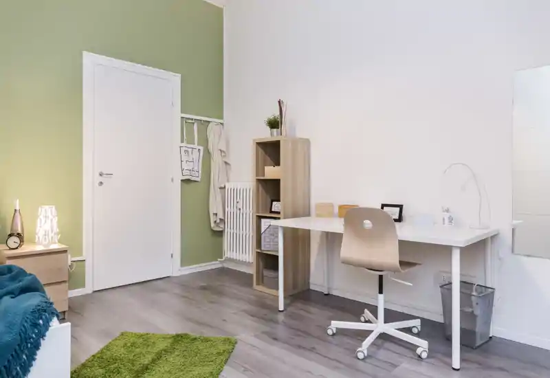 Coin chambre lumineux et moderne avec un bureau simple, une étagère et un espace table de chevet ; mobilier en bois clair, mur accent vert et textiles doux pour une ambiance fraîche et reposante.