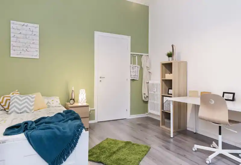 Chambre lumineuse et bien rangée avec lit, table de chevet et espace bureau ; textiles doux et mur vert apportent une ambiance apaisante.