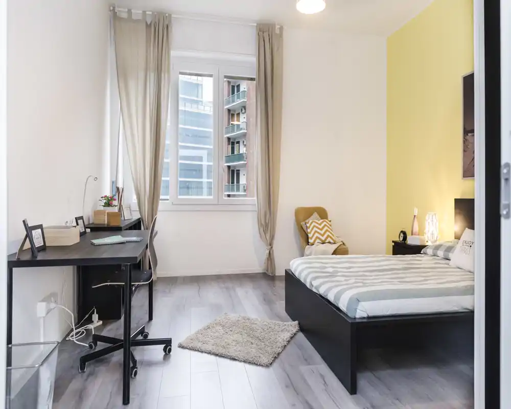 Dormitorio moderno y luminoso con cama doble cómoda, zona de trabajo junto a la ventana, alfombra y butaca.