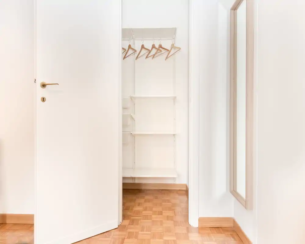 Ingresso luminoso e minimale con un piccolo armadio a muro, appendini in legno e pavimento in parquet — pulito e pronto all'uso.