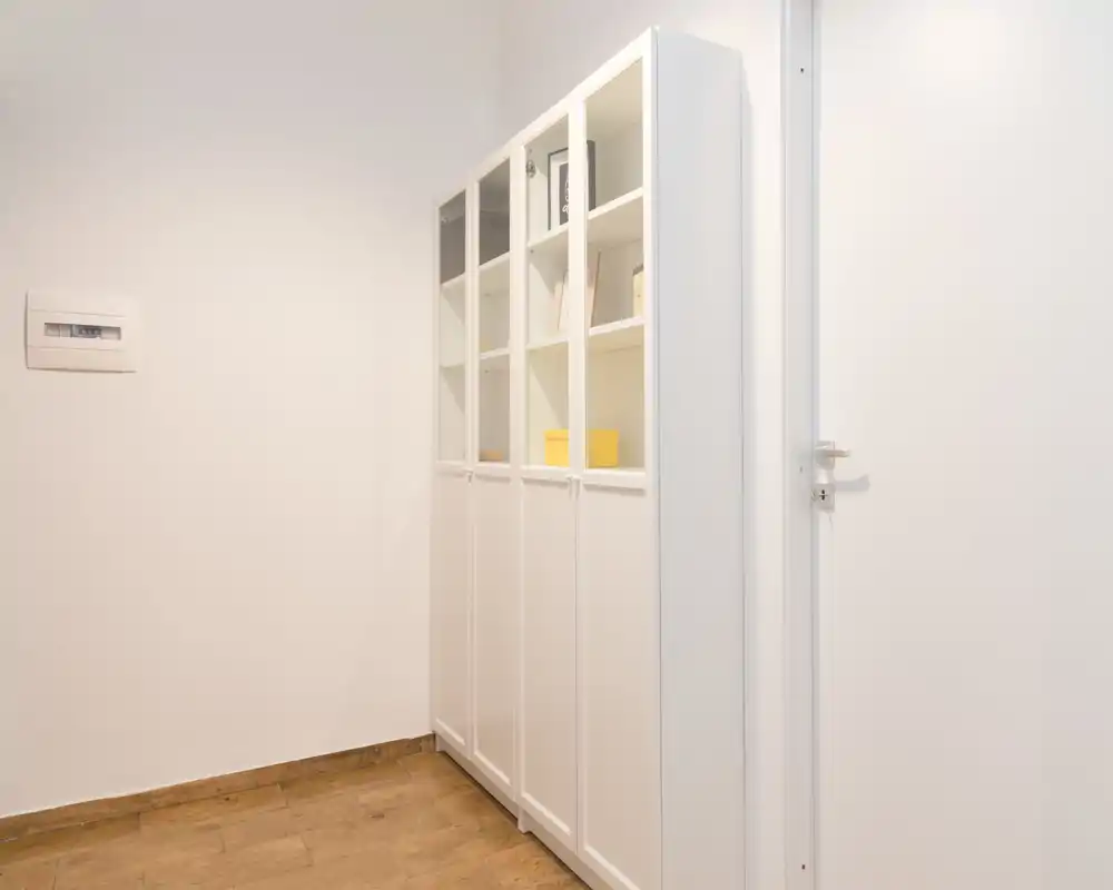 Entrada minimalista o pequeño pasillo con paredes blancas, suelo de madera y un armario alto blanco—luminoso y despejado.