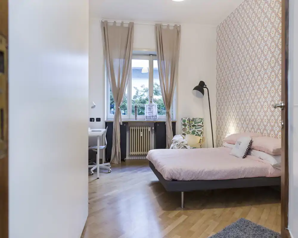 Dormitorio luminoso y con estilo, con cama de tamaño matrimonial, pared decorativa y una gran ventana que aporta luz natural. Lámpara de lectura y sillón crean un ambiente acogedor y moderno.