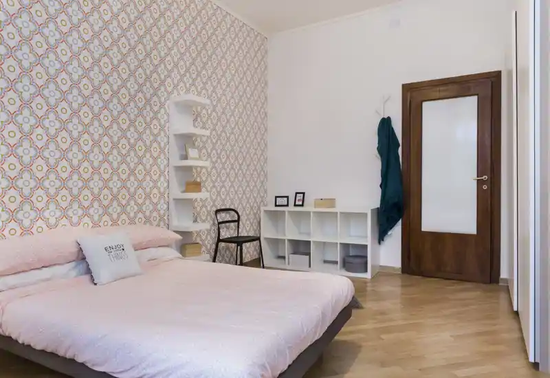 Dormitorio luminoso y ordenado con cama doble, pared decorativa y estanterías modulares — acogedor y bien iluminado.