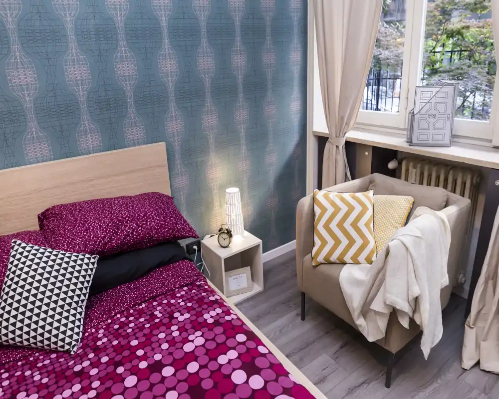 Dormitorio luminoso y cuidado con cabecero de madera, ropa de cama de diseño y un butacón acogedor junto a la ventana que aporta luz natural — perfecto para anuncios.