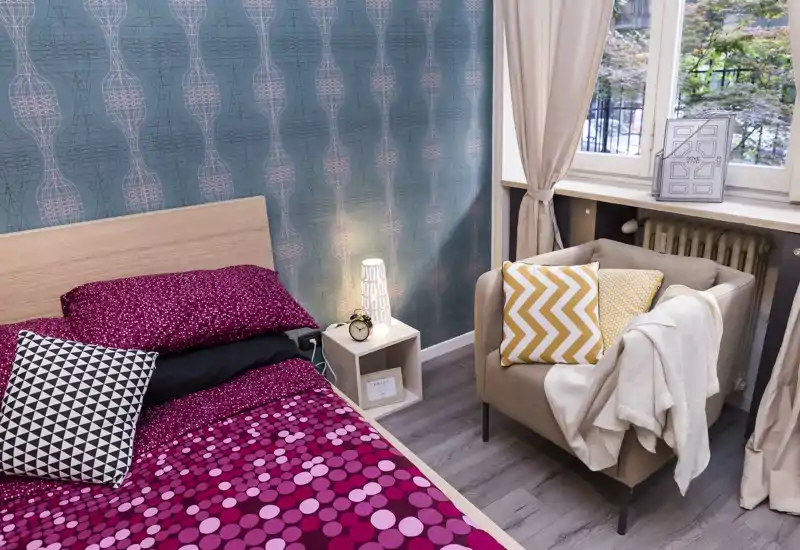 Dormitorio luminoso y cuidado con cabecero de madera, ropa de cama de diseño y un butacón acogedor junto a la ventana que aporta luz natural — perfecto para anuncios.