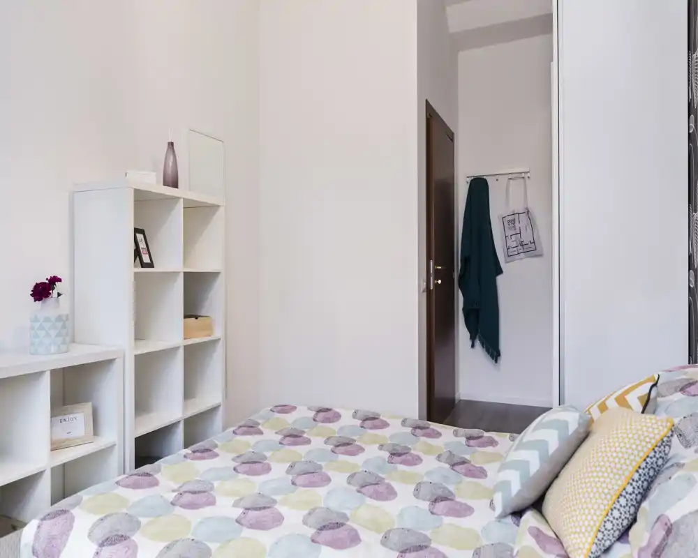Chambre lumineuse et bien décorée avec une couette à motifs et des coussins décoratifs ; étagères et déco minimaliste créent une ambiance moderne et apaisante, idéale pour une annonce.