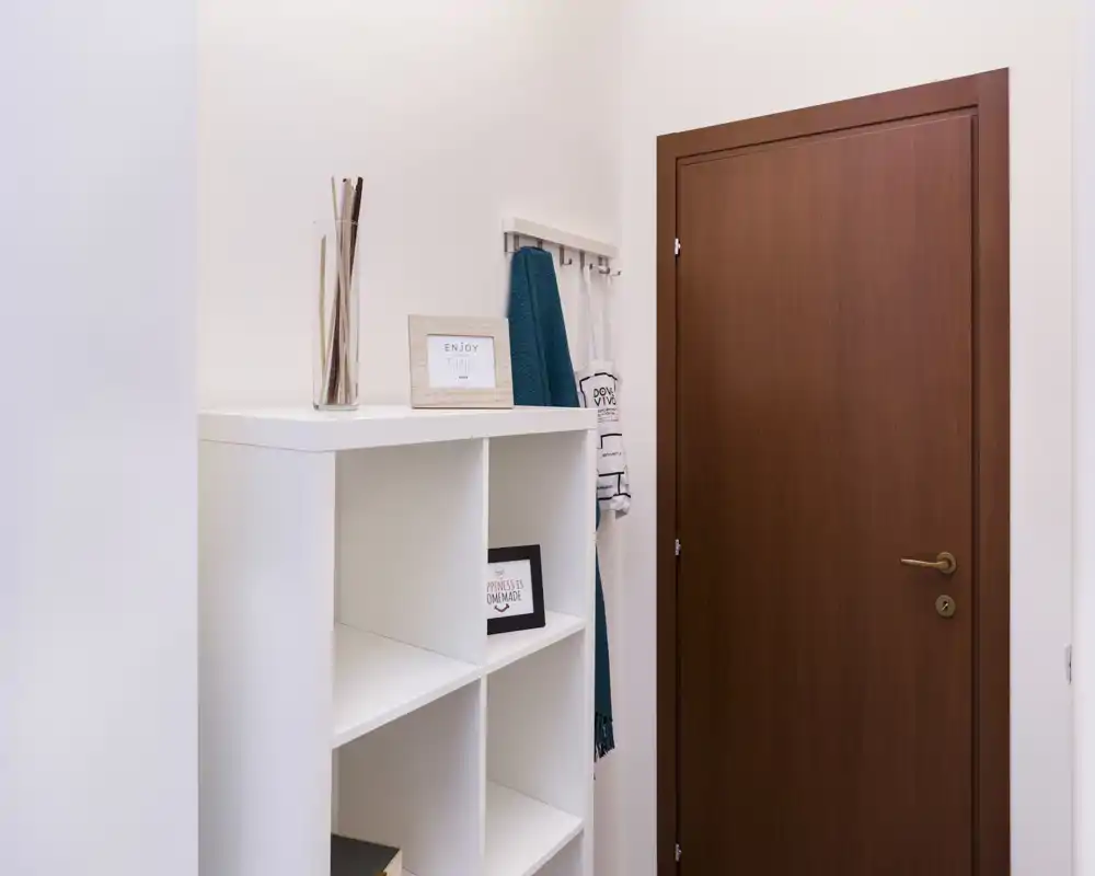 Pequeña entrada ordenada con puerta de madera, percheros de pared y un mueble cubo blanco — decorado de forma luminosa y minimalista, ideal para dar la bienvenida.