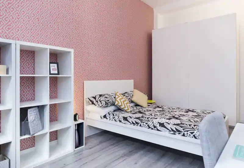 Dormitorio luminoso y con estilo, ropa de cama estampada, cojines decorativos y un armario grande. Líneas modernas, pared decorativa y estantería modular para almacenamiento práctico.
