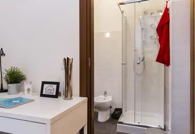Bagno compatto e moderno con box doccia in vetro, bidet e pavimento piastrellato; design luminoso e pulito, ideale per affitti brevi.