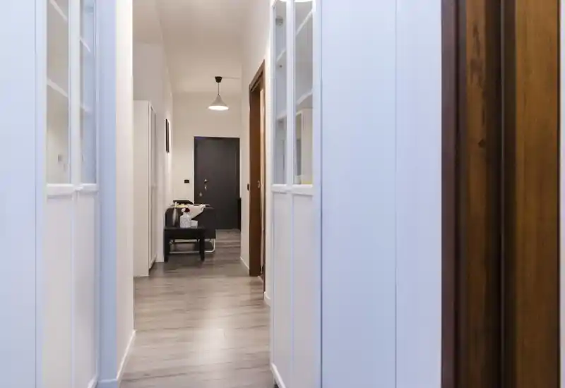 Ingresso moderno e luminoso con pavimento in legno chiaro, una panca e lampada a sospensione che conduce alla porta d'ingresso — corridoio pulito e accogliente.
