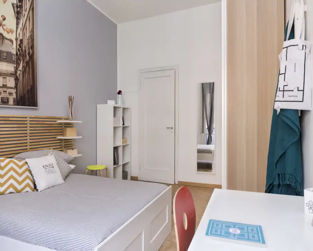 Camera da letto moderna e luminosa con letto matrimoniale ben rifatto, cuscini decorativi e una scrivania funzionale — perfetta per un soggiorno confortevole.