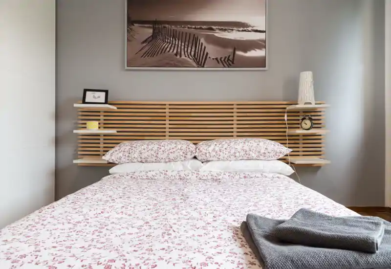 Dormitorio luminoso y bien decorado con cama grande, edredón estampado y cabecero de listones de madera; estantes junto a la cama y luz natural crean un ambiente tranquilo y acogedor.