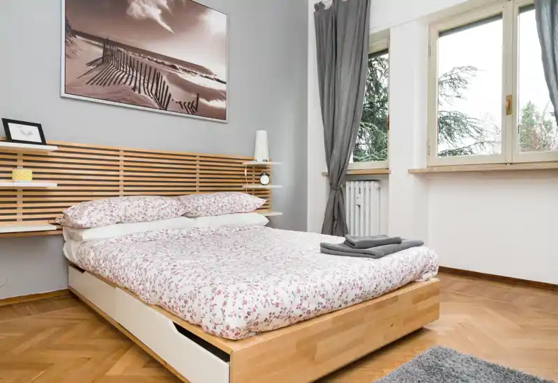 Dormitorio luminoso y limpio con cama de madera moderna, ropa de cama floral y grandes ventanas que aportan luz natural — un espacio acogedor y bien presentado, ideal para anuncios de alquiler.