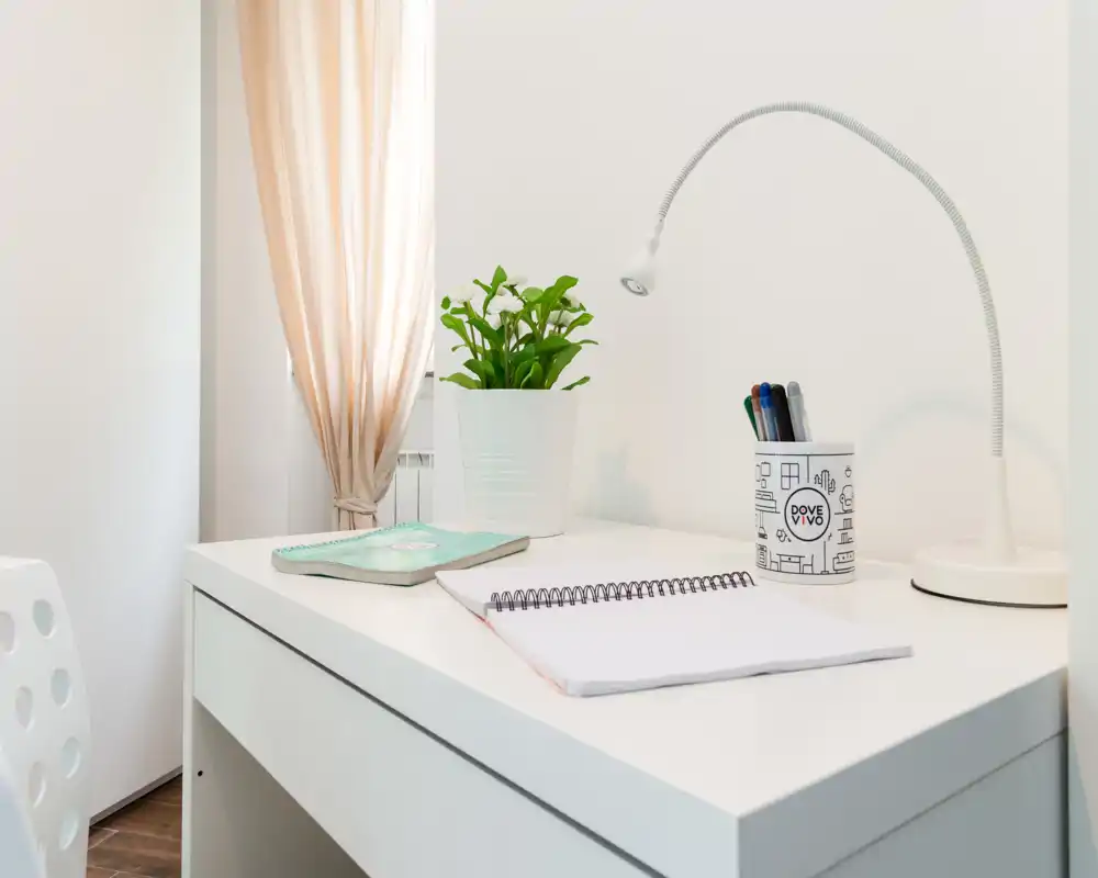 Bright, minimal workspace corner with a white desk, lamp, notebook and a small potted plant — ideal for studying or remote work.