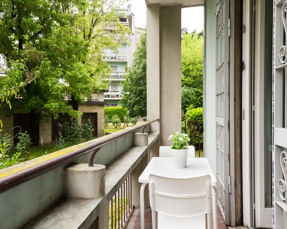 Sunny balcony with a small table and chairs overlooking a green courtyard — ideal for morning coffee or relaxing outdoors.