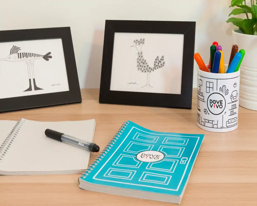 Gros plan sur un bureau en bois avec carnets, un stylo, des cadres décoratifs et un pot contenant des stylos colorés — un petit espace de travail propre, adapté à l'étude ou à l'accueil.