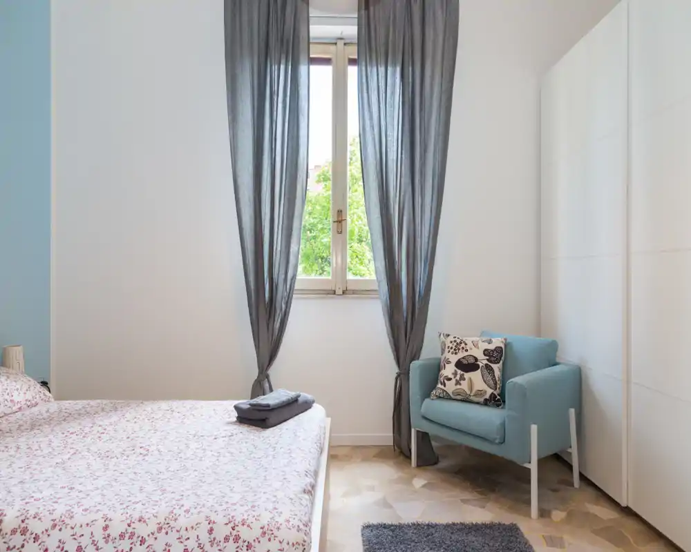 Chambre lumineuse et soignée avec un lit double à couette imprimée, un fauteuil confortable près de la fenêtre et une armoire intégrée — idéale pour un séjour reposant.