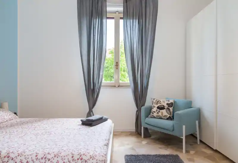 Chambre lumineuse et soignée avec un lit double à couette imprimée, un fauteuil confortable près de la fenêtre et une armoire intégrée — idéale pour un séjour reposant.