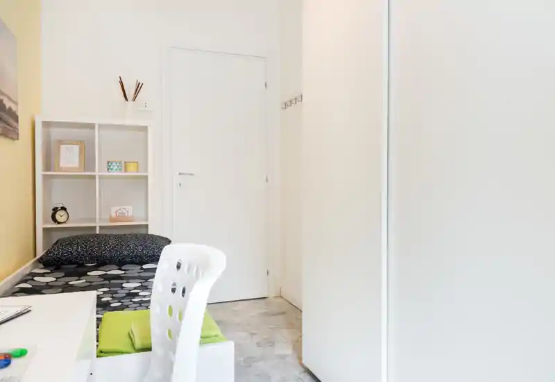 Petite chambre lumineuse avec un lit simple, des étagères épurées et un coin bureau bien rangé. Style minimaliste et lumière naturelle agréable, idéale pour une annonce de location.