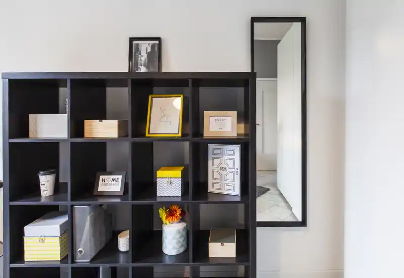 Una estantería moderna actúa como separador con cajas decorativas, marcos y un jarrón, aportando un detalle ordenado y contemporáneo del salón.